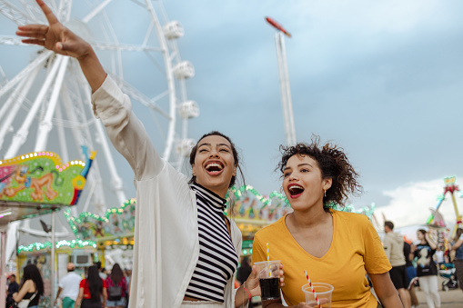 Portrait of happy friends having fun in the amusement park. They are talking and drinking. Behind them is a Ferries Wheel. Space for copy.