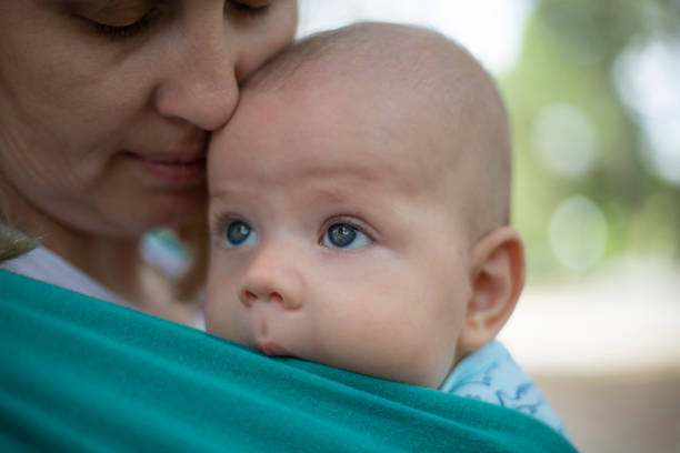 Close up shot of a young woman carrying a baby boy in a sling.