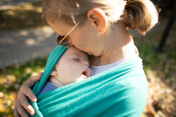 Above shot of a young woman carrying a baby boy in a sling and walking.