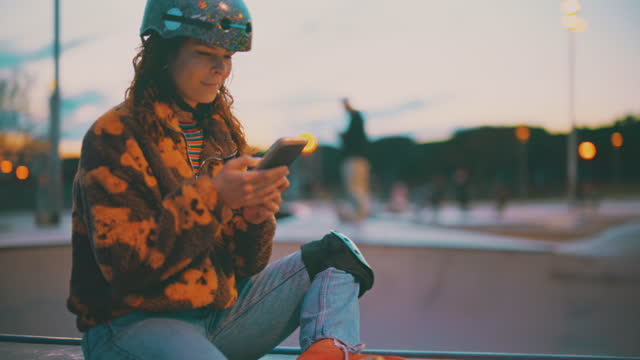 SLO MO Young female roller skater uses her smartphone at the skate park at dusk