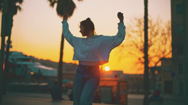 SLOW MOTION Young woman with double ponytails having fun roller skating among palm trees at sunset