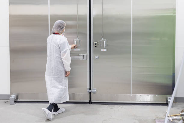 Female in white clean suit opening a large aluminum door stock photo