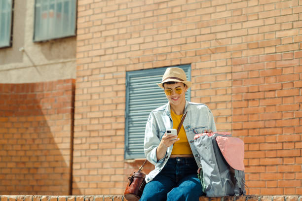 istock Beautiful woman sitting on the brick wall and using smart phone 1491363301