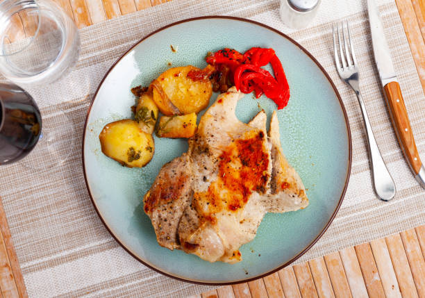 Slice of appetizing roasted pork shoulder with side dish of baked potatoes and pepper. Homemade dinner