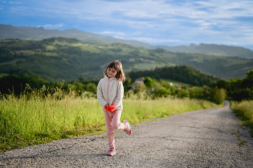 little girl standing on a country road and holding flowers.
