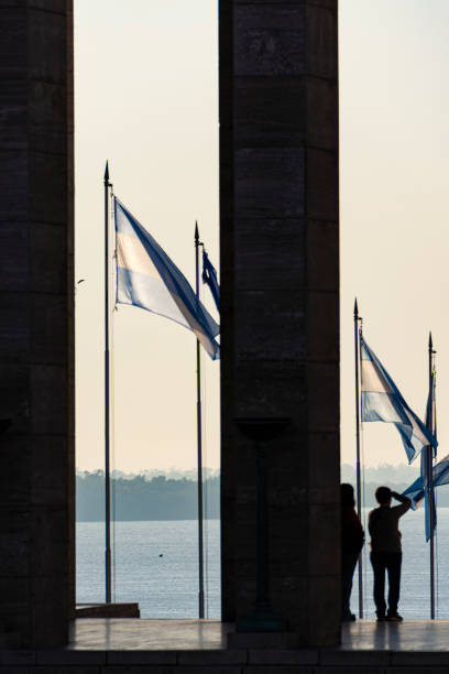 2人、アルゼンチンの旗、そして背景にパラナ川。アルゼンチン国旗記念碑。日2023年4月26日アーゴン州サンタフェ、ロザリオ市。 - bandera ストックフォトと画像