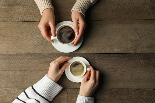 Women with cups of aromatic coffee at wooden table, top view. Space for text