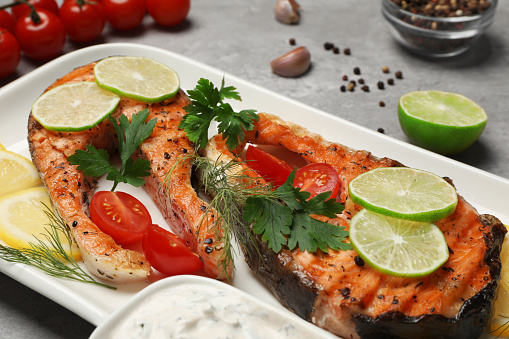 Tasty grilled salmon steaks and ingredients on light grey table