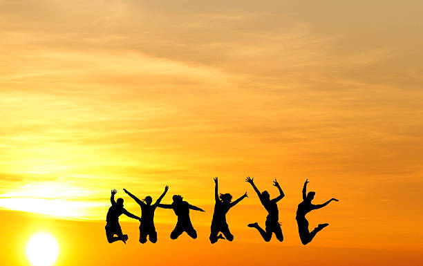 silhouette of female friends jumping in sunset stock photo