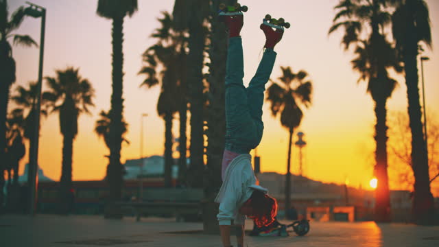SLO MO Young woman in roller skates performs acrobatic move - handstand in the city at sunset