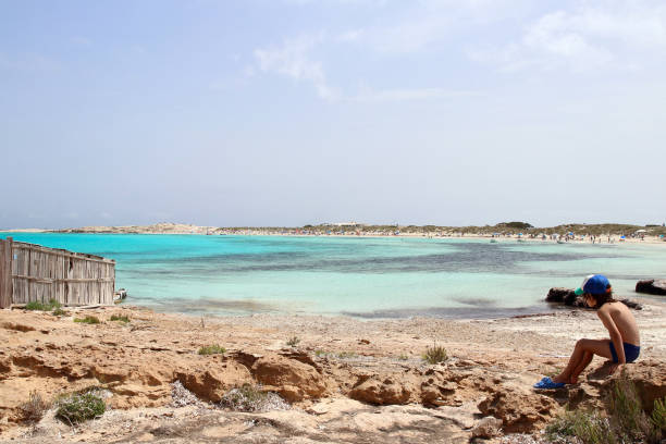 スペインのフォルメンテラ島で最も驚くべき象徴的なスポットの1つであるセスイリェテスビーチの海岸近くに座っている小さな子供 - illetes ストックフォトと画像