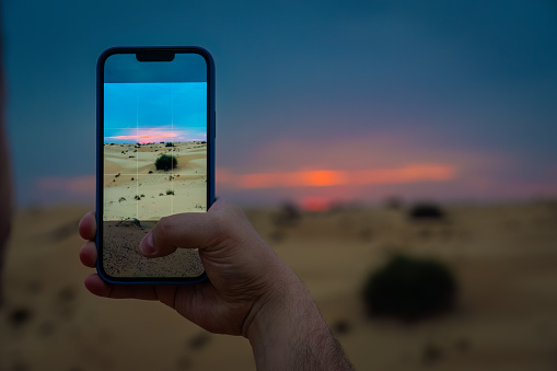 A young man takes a picture with his mobile phone of the desert outside Dubai at sunset.