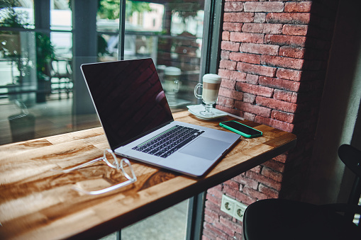 A laptop for remotely smart working by the window in a coffee shop. Cozy workplace