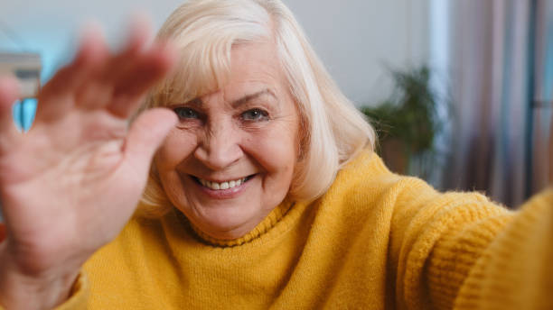POV senior grandmother woman making online selfie video call talking waving hand looking at camera POV of senior grandmother woman making online selfie video call talking waving hand looking at camera at home apartment indoors. Communication, meeting. Elderly blogger making smartphone conversation man video call pov stock pictures, royalty-free photos & images