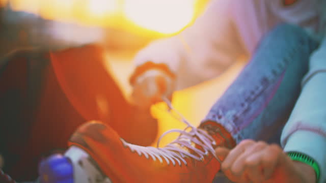 SLOW MOTION shot of young woman tying lace on rollerblades. Female is wearing roller skates. She is sitting at town square.