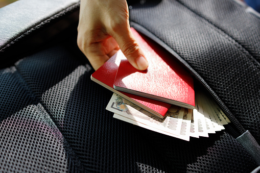 The cropped image shows a tourist keeping her passport and money in a safe compartment or pocket in her backpack to prevent pickpocketing while traveling