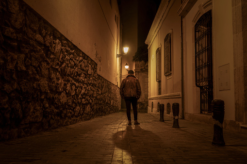 Rear view of adult man walking on street at night. Almeria, Spain