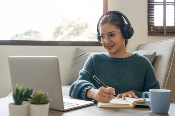istock woman taking notes in notebook while using laptop at home in living room. Focused lady writing in notepad 1491405902