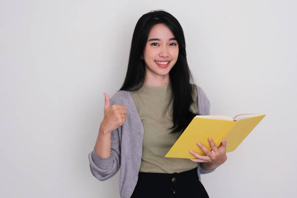 istock Young Asian woman smiling and give thumb up while holding a book 1491405979