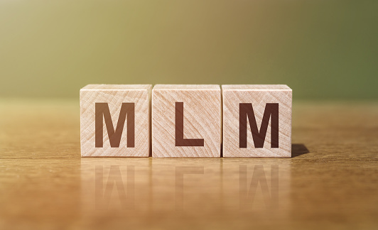 MLM (Multi-Level Marketing) word written on wooden blocks on wooden table. Concept for your design.