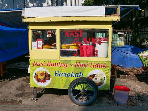 A traditional Indonesian Street Push Food Cart selling nasi kuning and nasi uduk in Bandung, West Java, Indonesia. Nasi kuning is yellow turmeric rice with assorted condiments and nasi uduk is coconut rice with condiments. Food carts usual sell this food in the morning time for breakfast.
