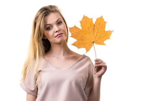 Fashionable autumn long hair blonde girl holding autumnal dry brown maple leaf in hand. Autumn, season and forecasting concept.