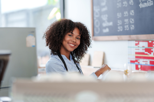 Successful young baristas woman standing in bar counter in cafe. Small startup business owner concept. Happy coffee shop woman waitress in an apron smiling confidently in a cafe.