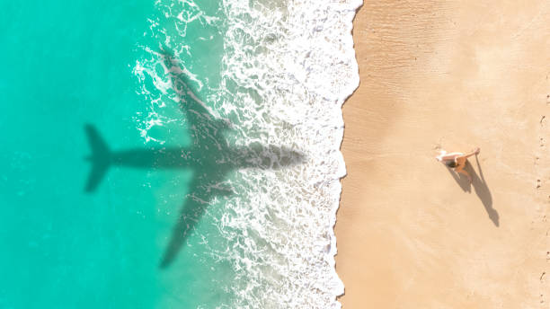 Airplane shadow flying over tropical beach. Airplane shadow flying over beautiful exotic tropical beach with woman sunbathing on a sunny cay - Summer vacation travel concept planes flying overhead stock pictures, royalty-free photos & images