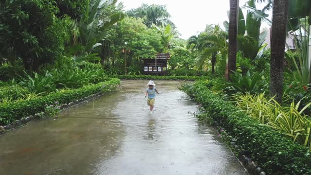 Happy little kid, laughing and running in rain and fun jumping into puddle. Joyful, enjoying nature