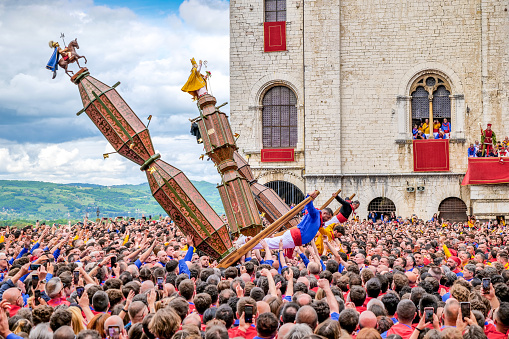 Gubbio, Umbria, Italy, May 15 -- A scene of the traditional and ancient Festa dei Ceri in the historic heart of the medieval town of Gubbio in Umbria. The celebration consists of a race of three wooden columns weighing almost 300 kg each, called Ceri, carried on the shoulders of dozens of bearers, on top of which are placed the statues of Sant'Ubaldo (Saint Ubaldo) protector of Gubbio, San Giorgio (Saint George) and Sant'Antonio Abate (Saint Anthony). The race develops along the streets and alleys of Gubbio up to the summit of Monte Ingino where the Basilica of Sant'Ubaldo is located. This religious celebration, much loved by the whole community of Gubbio, is considered one of the oldest in Italy and in the world and its origins date back to the 12th century. In the photo: The leaders of the bearers rush forward to raise the three wooden columns of the Ceri to start the race. Image in high definition quality.