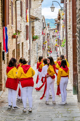 Gubbio, Umbria, Italy, May 15 -- A scene of the traditional and ancient Festa dei Ceri in the historic heart of the medieval town of Gubbio in Umbria. The celebration consists of a race of three wooden columns weighing almost 300 kg each, called Ceri, carried on the shoulders of dozens of bearers, on top of which are placed the statues of Sant'Ubaldo (Saint Ubaldo) protector of Gubbio, San Giorgio (Saint George) and Sant'Antonio Abate (Saint Anthony).\nThe race develops along the streets and alleys of Gubbio up to the summit of Monte Ingino where the Basilica of Sant'Ubaldo is located. This religious celebration, much loved by the whole community of Gubbio, is considered one of the oldest in Italy and in the world and its origins date back to the 12th century. In the photo: A group of women participating in the Festa dei Ceri along a stone alley in the medieval heart of Gubbio. Image in high definition quality.