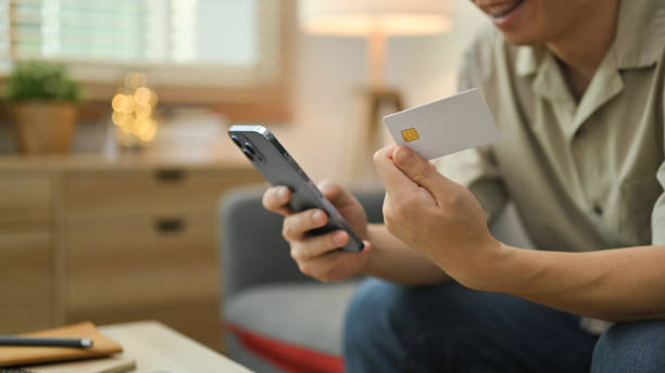 istock Man holding credit card and using mobile phone, making online transactions, shopping online at home. 1491438152