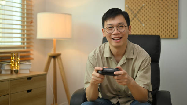istock Man in casual clothes and glasses holding wireless controller playing video game. Entertainment, technology and hobby concept. 1491438175