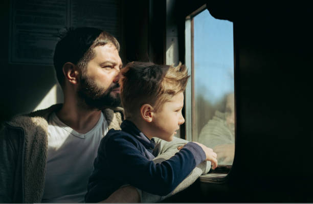 pai e filho sentados à janela no trem. conceito de viagem - evacuação e relocação - fotografias e filmes do acervo