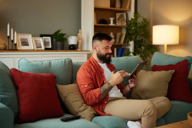 istock Tattooed man sitting on sofa using digital tablet at home 1491438753
