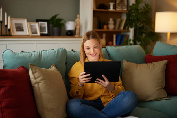 istock Relaxed woman sitting on sofa using digital tablet at home 1491438855