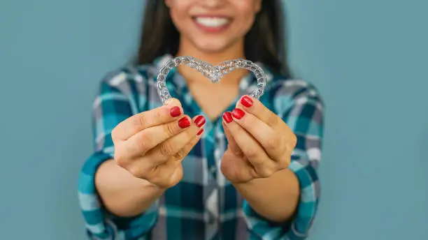 Photo of Young Asian Indian woman holding removable invisible aligner, also known as invisalign or  clear aligner