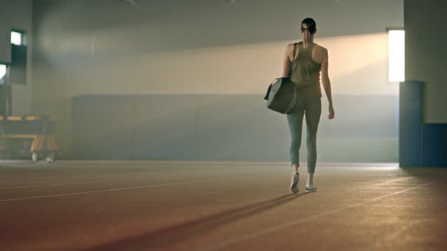 SLO MO LD Female athlete carrying a bag and leaving the gym after practice