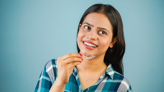 Young Asian Indian woman holding removable invisible aligner, also known as invisalign or  clear aligner