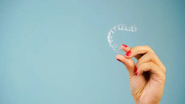 Photo of Young Asian Indian woman holding removable invisible aligner, also known as invisalign or  clear aligner