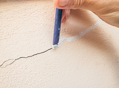 Repairing with stucco a crack in the wall plaster. Close-up of one hand and one tool