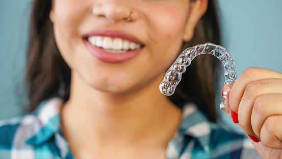 Young Asian Indian woman holding removable invisible aligner, also known as invisalign or  clear aligner