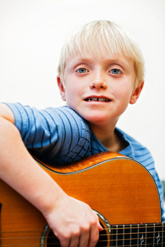 This handsome 7 year old boy gazes confidently out as he strums his acoustic guitar. Shot with Canon EOS 1Ds Mark III. 