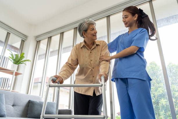 Young physical therapist female help aged female patient walk with walker Asian Young physical therapist female help aged female patient walk with walker at home, aftercare and physiotherapy concept walking aide stock pictures, royalty-free photos & images