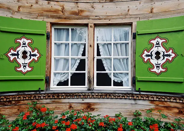 A charming chalet in Switzerland features a window with painted shutters and a flower box.