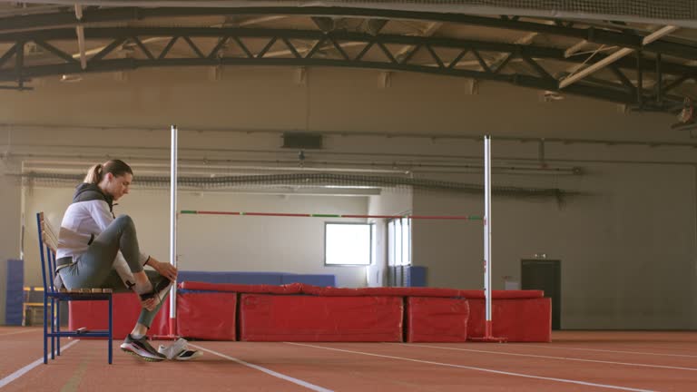 TS Female high jump athlete walking into the gymnasium and sitting on the bench