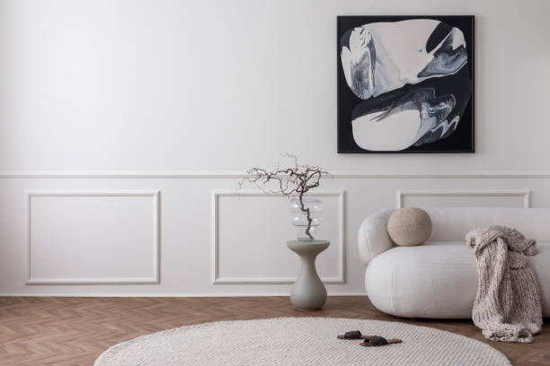 istock Minimalist composition of modern living room interior with mock up poster frame, copy space, beige sofa, round rug, stylish coffee table, vase with branch and personal accessories. Home decor Template 1491447511