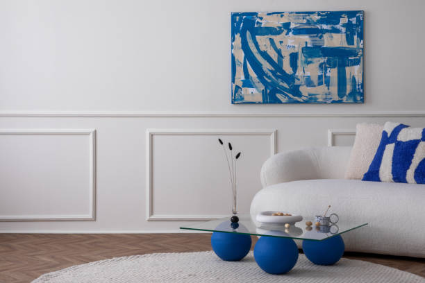 istock Modern composition of living room interior with copy space, mock up poster frame, stylish sofa, glass coffee table, blue pillow, bowl with nuts, round rug and personal accessories. Home decor Template 1491447532