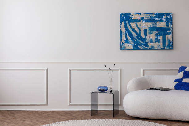 Modern composition of living room interior with copy space, mock up poster frame, stylish sofa, glass coffee table, blue pillow, bowl , round rug and personal accessories. Home decor Template