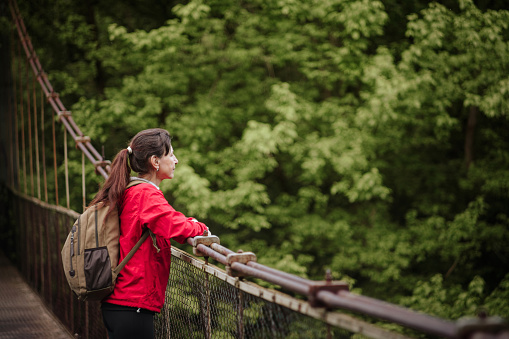 Mature woman hiking in nature standing on a suspension bridge